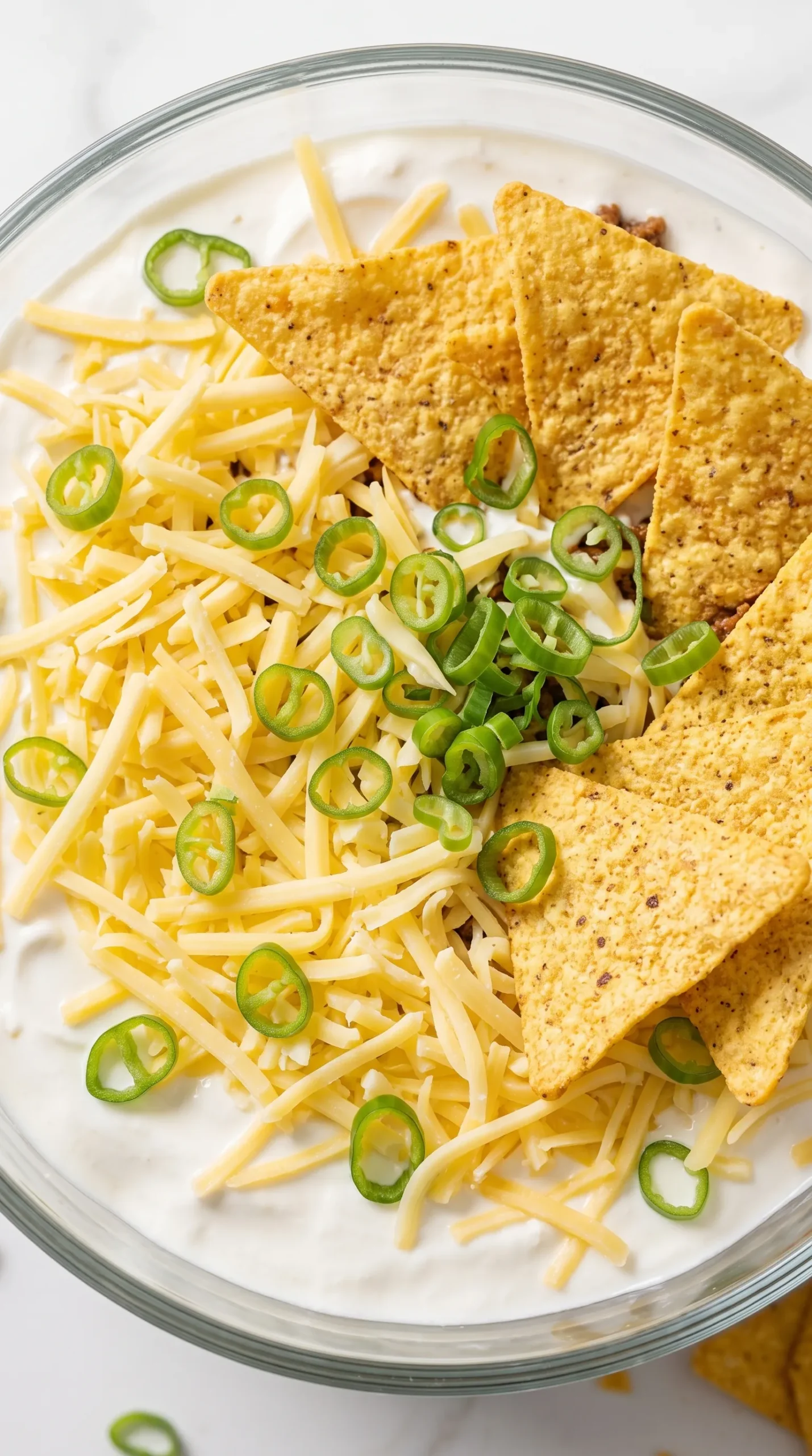 Nahaufnahme von Schicht-Taco-Salat — geriebener Gouda, Hackfleisch, Schmand und knusprige Chips